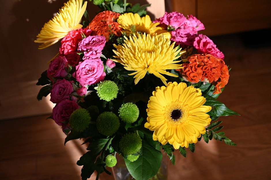 A vibrant floral arrangement featuring a mix of fresh flowers, including bright yellow gerbera daisies, large yellow chrysanthemums, pink roses, orange carnations, and small green pom-pom chrysanthemu