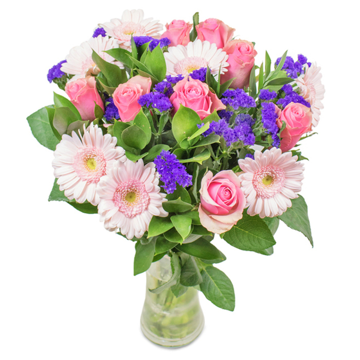 An elegantly crafted bouquet sits gracefully within a slender, clear glass vase, its arrangement speaking to the refined floral sensibility of Vauxhall. The central focus features approximately seven to nine soft to medium pink roses, their petals in various states of unfurling-some tightly coiled, others gently opening into classic spiral forms-imbuing the arrangement with a sense of romance and anticipation. Encircling these are five to seven pale pink gerbera daisies, their large, round heads and delicately radiating petals softening the bouquet's tone, while their near-white centers add a gentle luminosity. Bursts of vivid purple statice, reminiscent of the vibrant colour found in local Vauxhall flower markets, are cleverly interwoven throughout, offering a touch of depth and striking textural contrast. Deep green foliage grounds the ensemble with a lush base, echoing the abundant greenery along the river's edge, its freshness palpable and inviting. Visible stems and crystalline water within the transparent vase complete the natural aesthetic, suggesting both freshness and authenticity. This visually captivating combination-pink roses, gerbera daisies, and lively purple statice-is suited for myriad occasions, from birthdays and anniversaries to Mother's Day or as a sophisticated accent in a Vauxhall office or home, embodying joy, affection, and the enduring beauty of a considered floral gift delivered locally.
